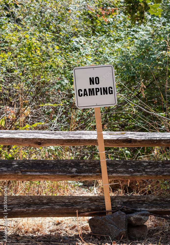 No camping sign beside fenced forest area