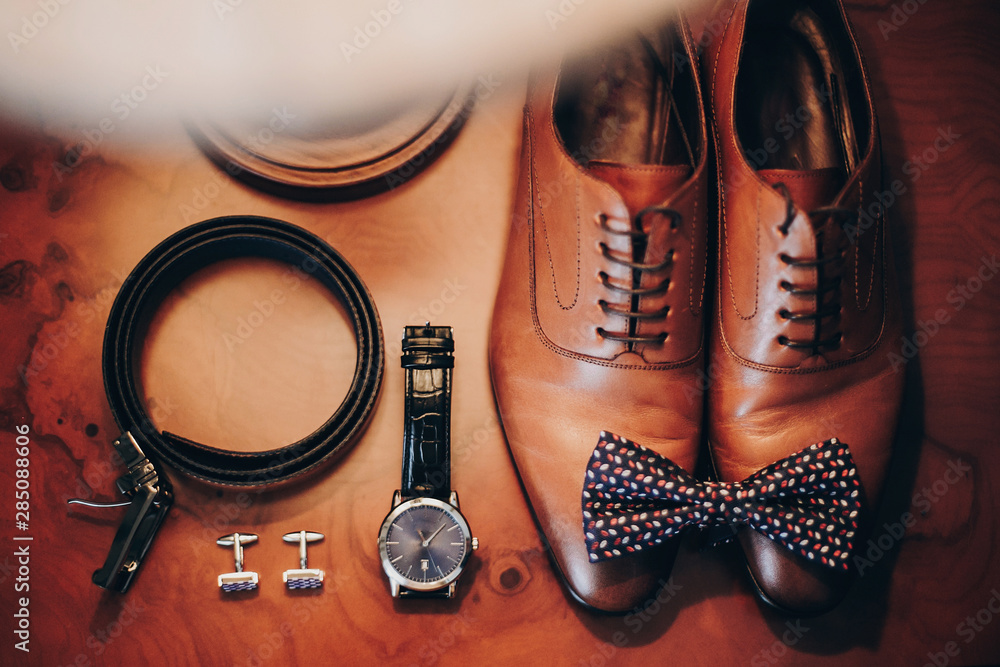 Stylish watch, expensive, shoes, bow tie, cufflinks and belt for groom on wooden table in hotel room. Morning preparation before wedding ceremony. Men accessory for luxury event - obrazy, fototapety, plakaty 