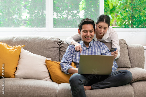 Couple online shopping at home in living room sofa. Asian man and woman, looking at computer.
