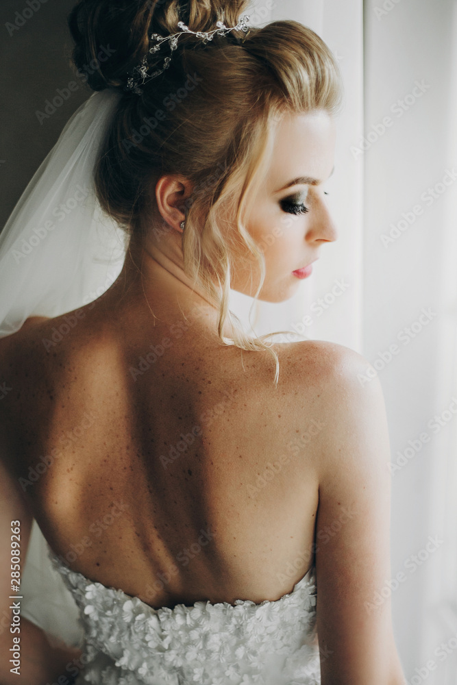 Stylish bride posing in soft light near window balcony in hotel room. Gorgeous sensual bride portrait. Morning preparation before wedding ceremony Stylish bride posing in soft light near window balcony in hotel room. Gorgeous sensual bride portrait. Morning preparation before wedding ceremony
