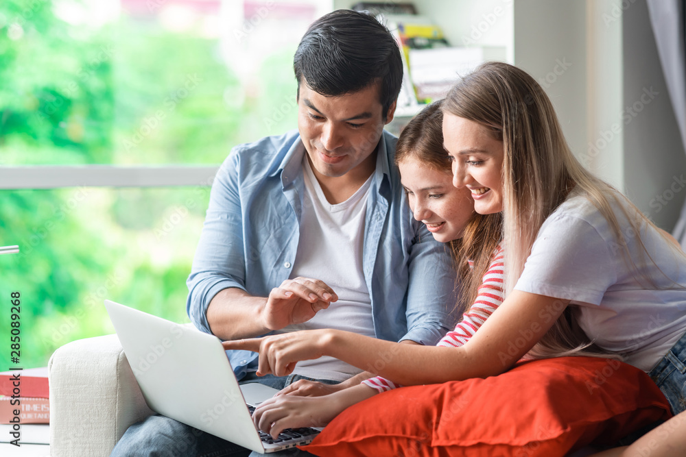 Girl learning how to use a computer with parents on sofa at home. Caucasian family. Mother teaching her. Girl learning how to use a computer with parents on sofa at home. Caucasian family. Mother teaching her.