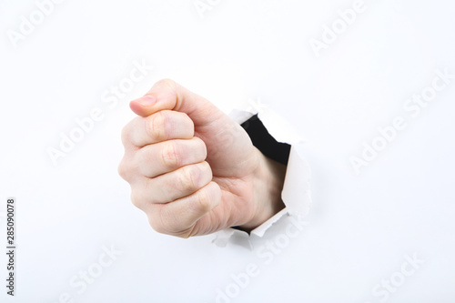 Hand shows fist from white torn paper