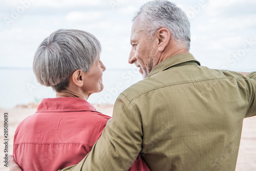 back view of senior couple embracing and looking at each other at beach