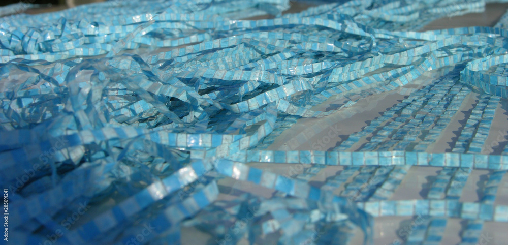 Obraz premium fragments of old blue polyethylene tarpaulin lie randomly on the metal surface. the wind and the sun (element) fancy mixed stripes tarpaulin between them. close up. shallow focus.