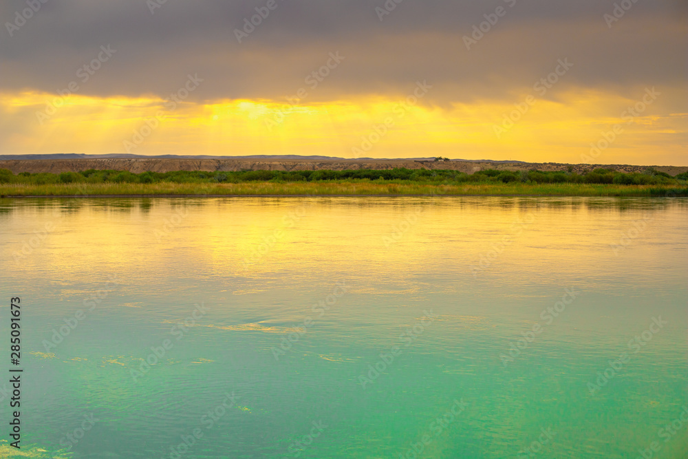 River with at sunset. Contrasting sky over the river. Golden rays of the sun at sunset. Pure blue mountain river river. Summer in Kazakhstan.