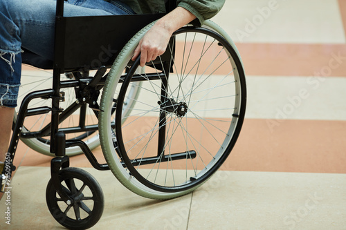 Close-up of young disabled woman sitting in wheelchair and going along the corridor