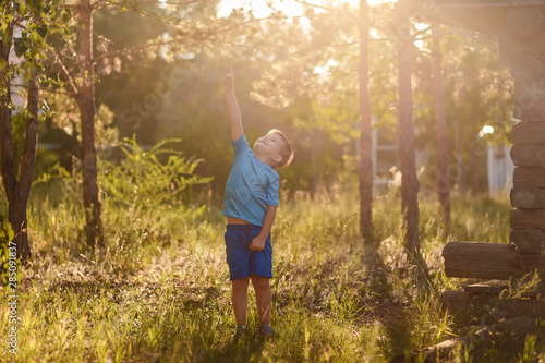 five-year-old Caucasian boy in a blue t-shirt and shorts stands in the sunlight in the summer in nature © Alyona