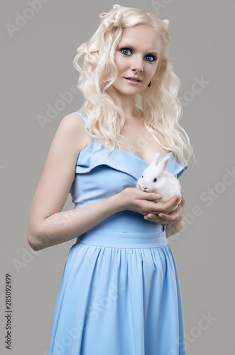 Albino blond girl in elegant dress posing with cute little rabbit