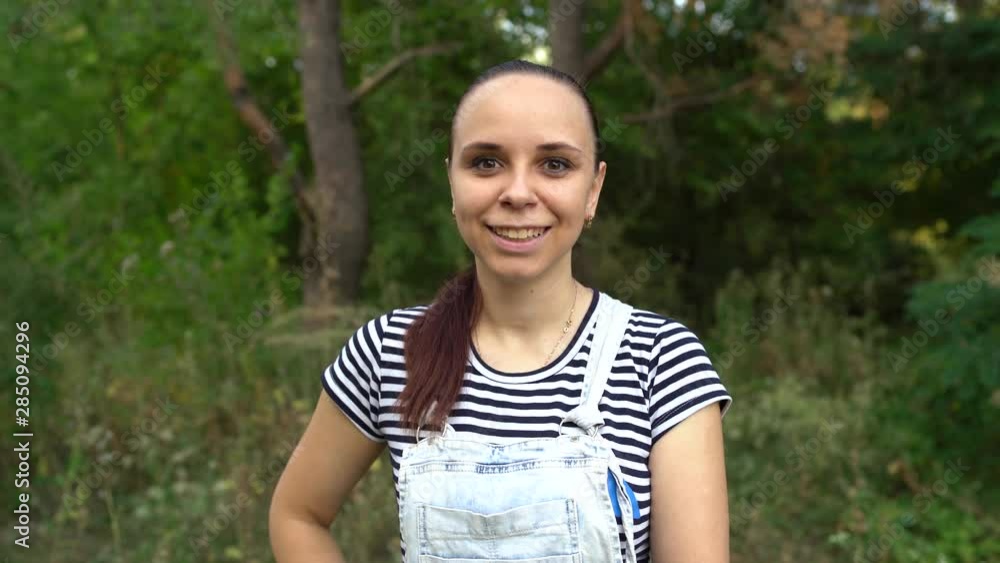 A young woman in casual clothes is smiling and showing her tongue looking at camera in the forest. A young woman in casual clothes is smiling and showing her tongue looking at camera in the forest.
