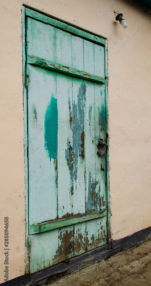 Old wooden dirty door in turquoise color. Decrepit requiring repair. Despondency in the interior. Side angle vertical frame