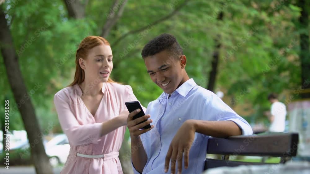 Offended teen girl noticing her boyfriend chatting smartphone in park, jealousy Offended teen girl noticing her boyfriend chatting smartphone in park, jealousy