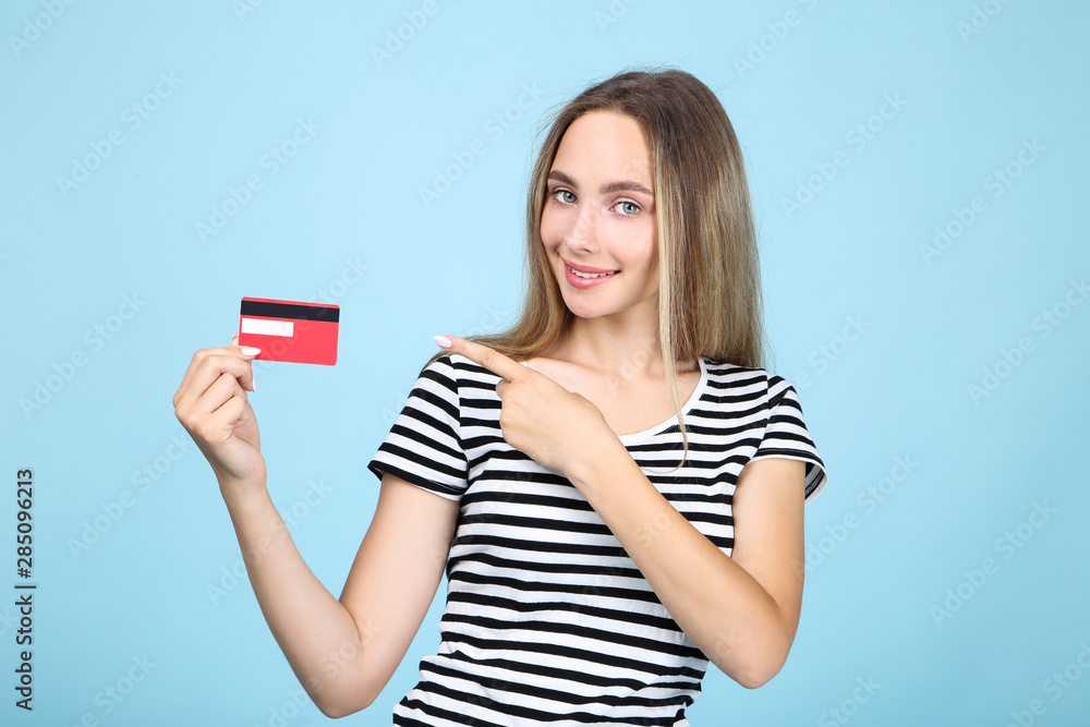 Beautiful young woman holding credit card on blue background Beautiful young woman holding credit card on blue background