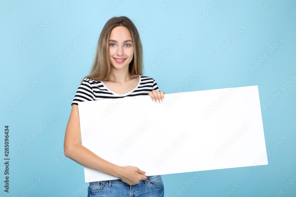 Beautiful young woman holding white blank board on blue background