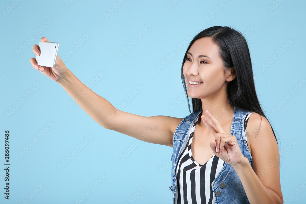 Young woman making selfie on smartphone on blue background Young woman making selfie on smartphone on blue background