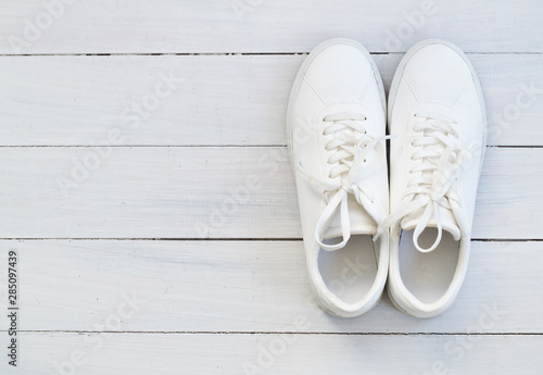 Fashion blog or magazine concept. White female sneakers on wooden background. Flat lay, top view minimal background.