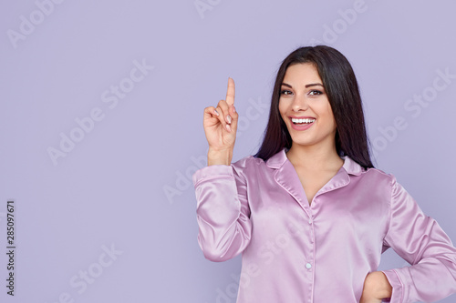Cheerful young woman in pajamas pointing finger upwards