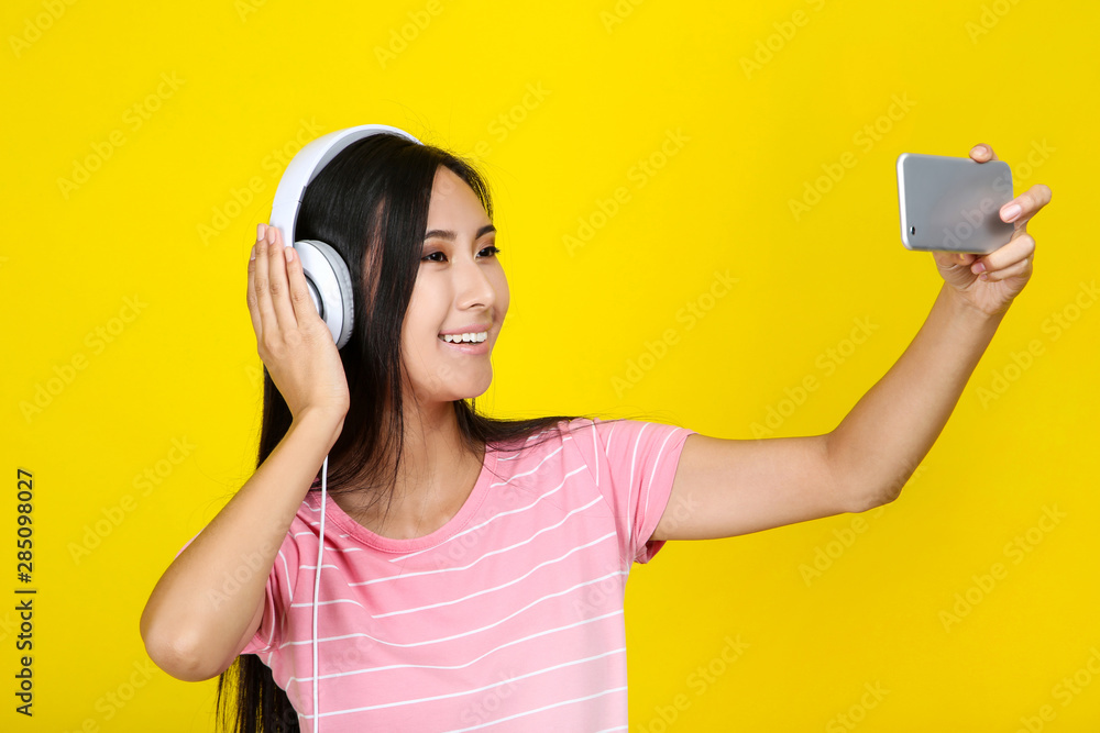 Young woman with headphones making selfie on smartphone on yellow background Young woman with headphones making selfie on smartphone on yellow background