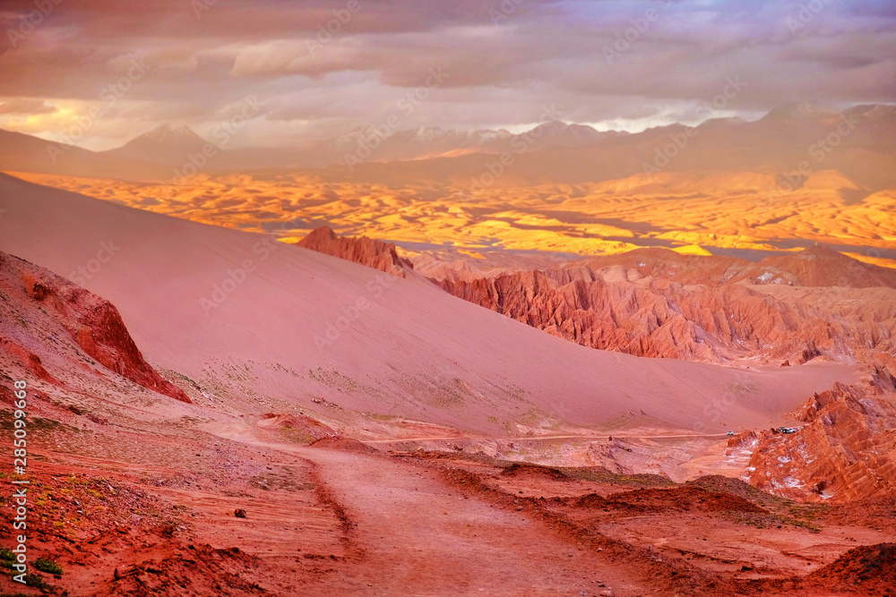 Fototapeta premium Panoramic view of the Mars Valley near San Pedro de Atacama against a warm and colorful sunset sky above volcanoes.