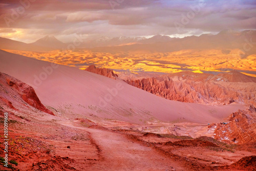 Panoramic view of the Mars Valley near San Pedro de Atacama against a warm and colorful sunset sky above volcanoes.