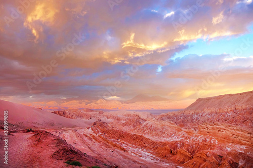 Panoramic view of the Mars Valley near San Pedro de Atacama against a warm and colorful sunset sky above volcanoes.