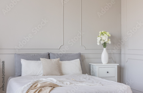 Flowers on white wooden nightstand table in luxury bedroom interior with king size bed