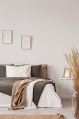 Graphics in wooden frames on white empty copy space wall in bedroom with comfortable bed with black and grey pillows and duvet