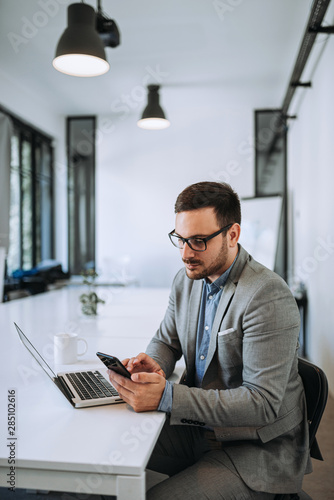 Caucasian businessman in casual wear checking messages on cellphone in office.