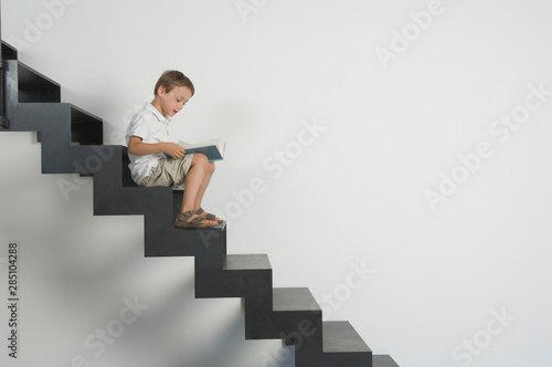 Germany, Boy years sitting on stairs and reading book photo