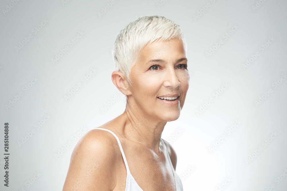 Beautiful smiling senior woman with short gray hair posing in front of gray background. Beauty photography. Beautiful smiling senior woman with short gray hair posing in front of gray background. Beauty photography.