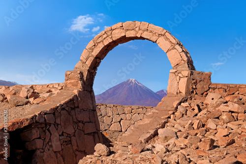 Desert landscape of volcano seen through arch in Pukara de Quitorand near San Pedro de Atacama, Chile, against a blue sky. photo