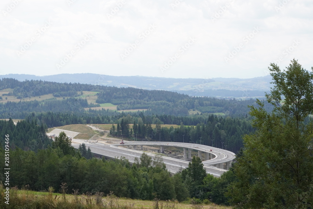 Naklejka premium construction of a modern overpass in mountains, high-speed concrete road in a mountainous area, a lot of tall trees on the slopes