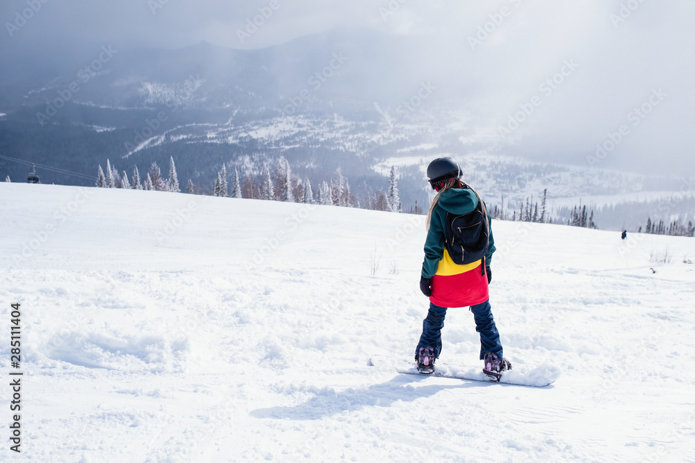 Girl with snowboard in the mountains walking on a snowy slope.