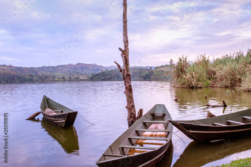 View of a wooden boats and big dry tree growing on Lake Nyabikere, with and the reflections on the water at sunrise, Rweteera, Fort Portal, Uganda, Africa photo