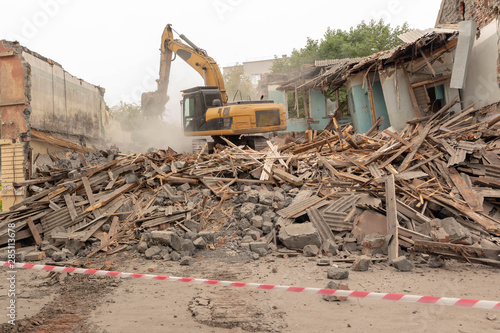Dismantling (demolition) of an old, dilapidated residential building. Excavator demolishes a house with a bucket.