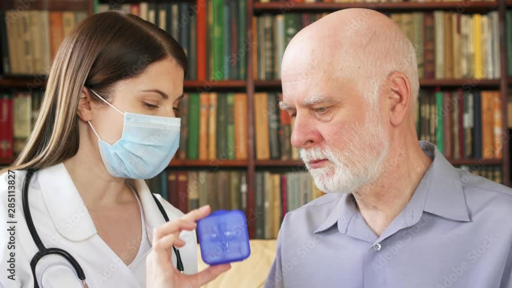 Female professional doctor in white coat and medical mask with stethoscope at work. Woman physician talk to sick senior male patient at home consult about new drug. Showing case of pills capsules Female professional doctor in white coat and medical mask with stethoscope at work. Woman physician talk to sick senior male patient at home consult about new drug. Showing case of pills capsules