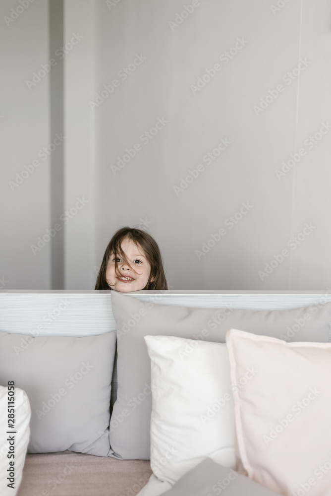 Little girl peeking out bed headboard Little girl peeking out bed headboard