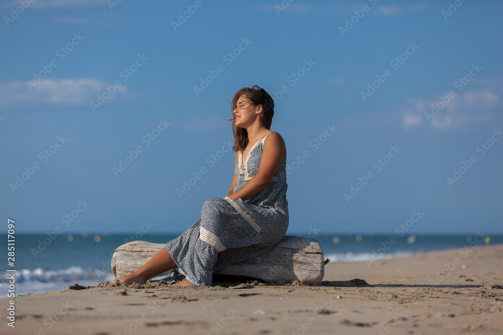 Young woman sitting on driftwood on the beach. Happiness Lifestyle Concept..