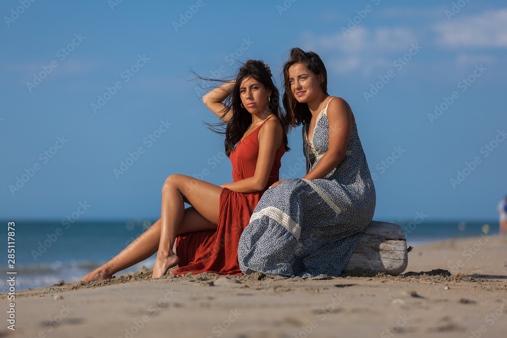 Complicity of two friends girls sitting on driftwood on the beach. Happiness Lifestyle Friendship Concept..