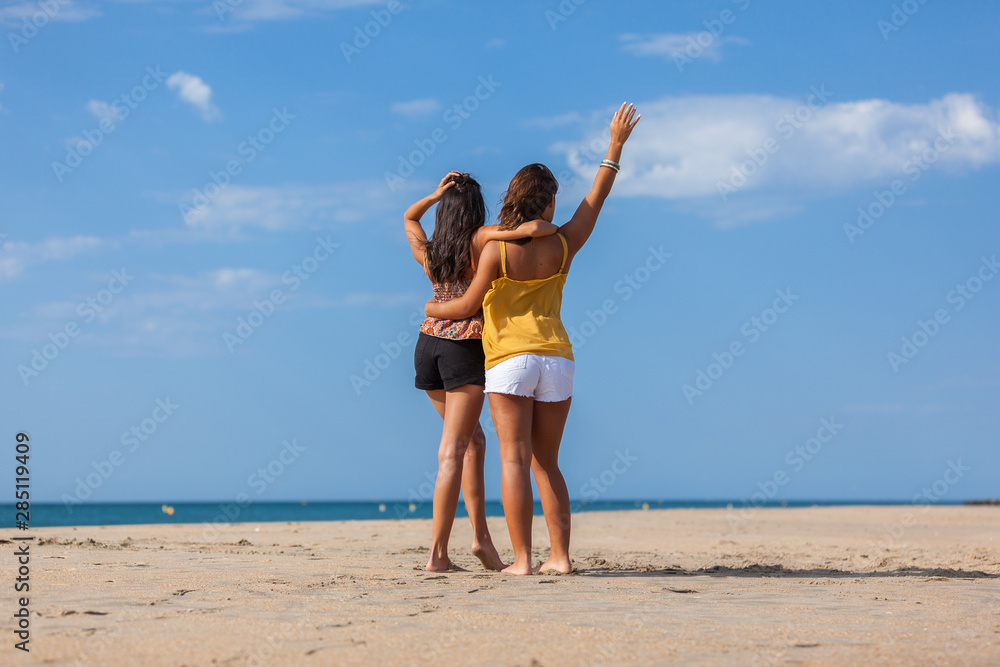 Complicity moment beetwen two girls best friends at the beach. Beautiful young women facing the sea.. Complicity moment beetwen two girls best friends at the beach. Beautiful young women facing the sea..