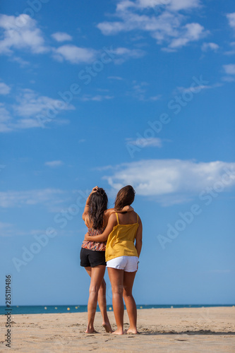 Complicity moment beetwen two girls best friends at the beach. Beautiful young women facing the sea..