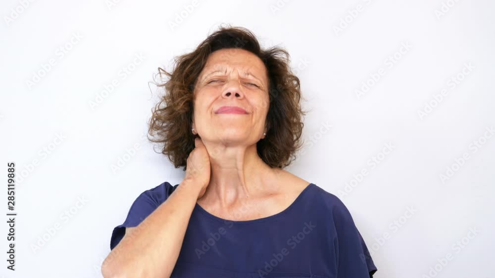Mature caucasian woman holding her neck behind as she having headache and feeling pain in the neck and back. Shot in 4K, white background Mature caucasian woman holding her neck behind as she having headache and feeling pain in the neck and back. Shot in 4K, white background