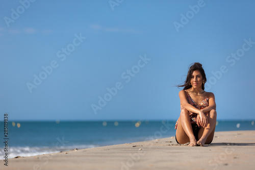 Calm young woman sitting alone on a sand beach. Relaxing and harmony concept..