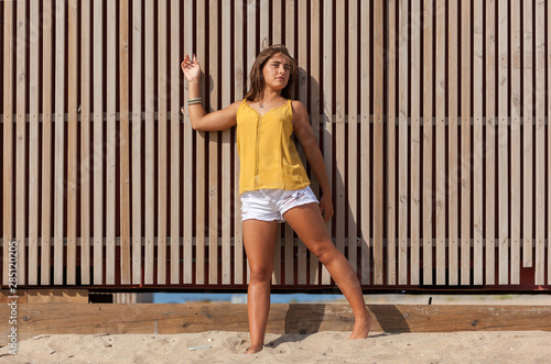Pretty young woman leaning against a wooden fence..Happy girl enjoying freedom in the sun at the beach.