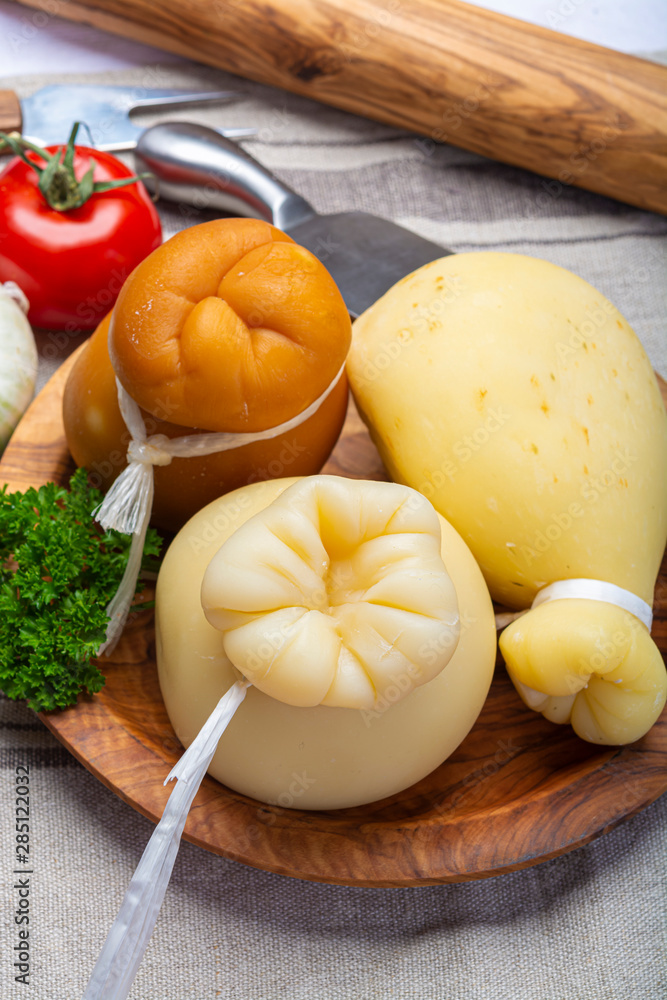 Italian provolone or provola caciocavallo hard and smoked cheeses in teardrop form served on olive tree board close up Italian provolone or provola caciocavallo hard and smoked cheeses in teardrop form served on olive tree board close up