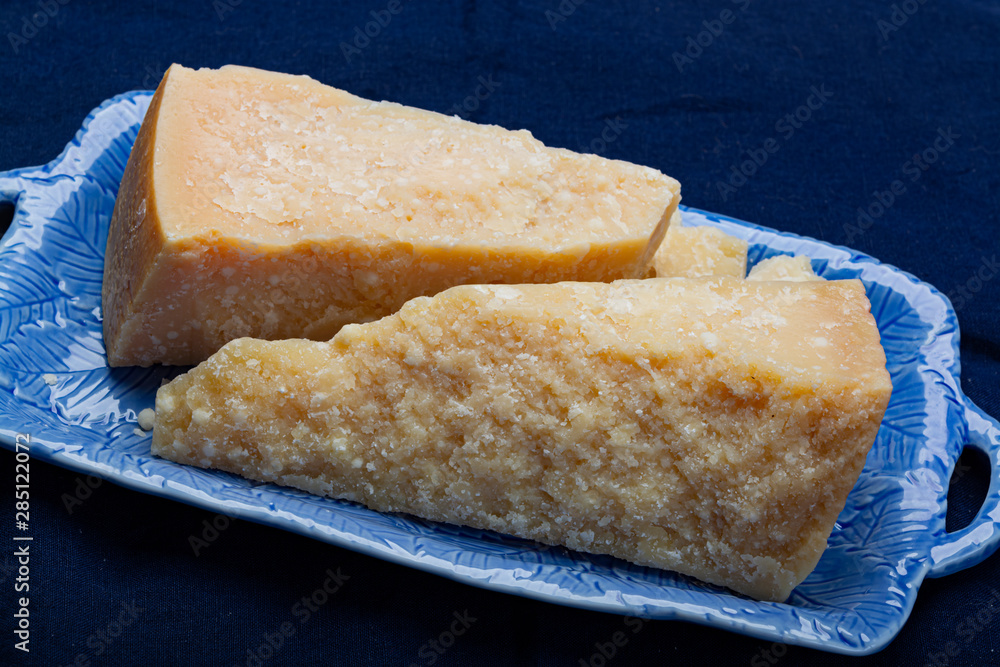 Italian original aged Parmesan cheese in two pieces served on blue plate close up Italian original aged Parmesan cheese in two pieces served on blue plate close up