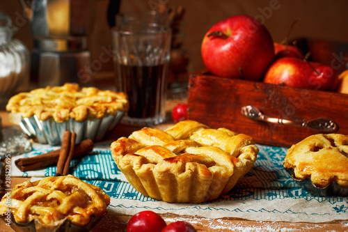 Mini homemade apple pies on rustic background with coffee,cinnamon sticks,apples,vintage towel