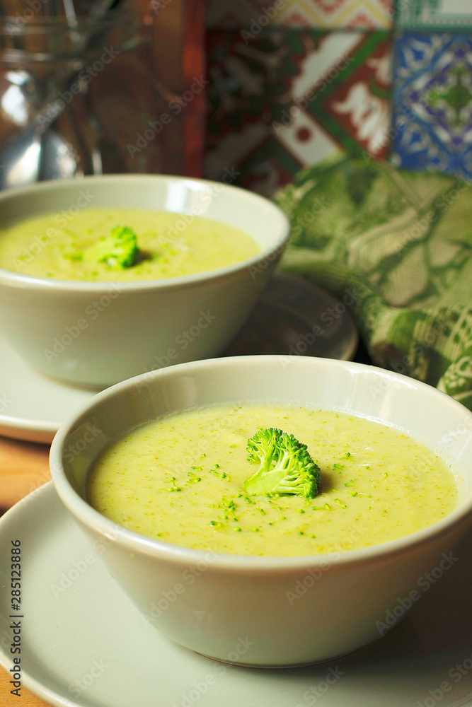 Fresh Broccoli cream soup on two gray ceramic bowl on plate with spoon on marble background,vegetarian food,healthy concept