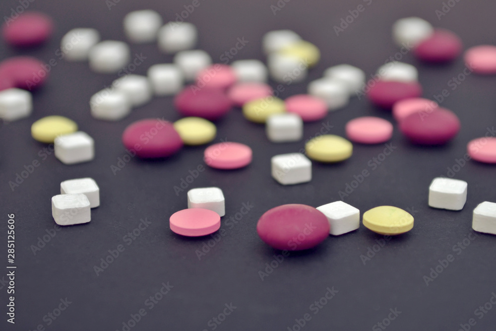 Pink, yellow round pills and white square are scattered randomly on a dark blue background, side view Pink, yellow round pills and white square are scattered randomly on a dark blue background, side view
