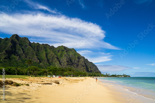 Kualoa Rock Beach on Oahu, Hawaii on a sunny day with some green mountains in the background.
