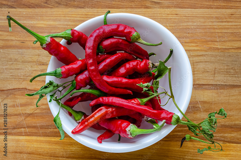 Bowl full of red chili peppers on a wooden cutting board Bowl full of red chili peppers on a wooden cutting board